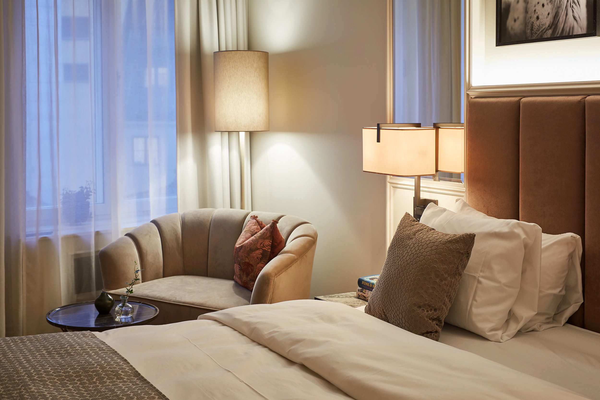 Modernt hotellrum med dubbelsäng, fåtölj vid fönster och varm belysning i stilfull hotellinteriör